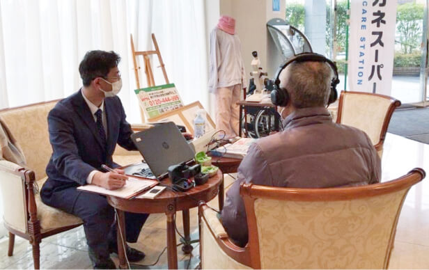 施設の相談会でヘッドホンを着けた男性の聴力をチェックするスタッフ